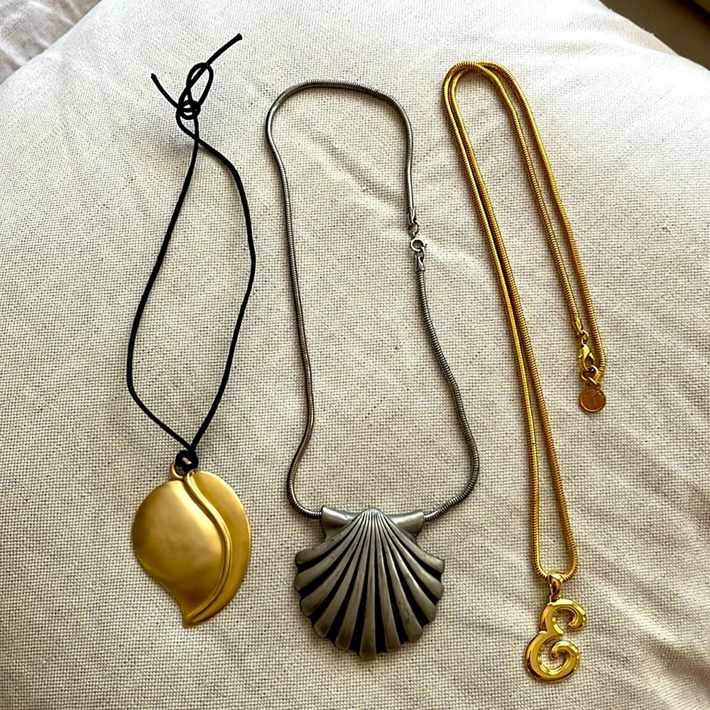 Three gold and silver pendant necklaces: gold E, silver shell and gold leaf.